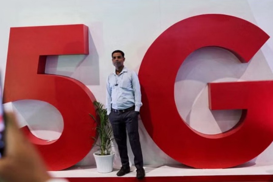 A man takes a picture of a friend in front of a sign showing installation of the 5G network in New Delhi, India, October 3, 2022. REUTERS