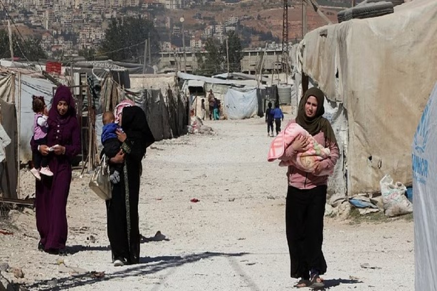 Syrian refugee women carry children as they walk at an informal camp, in the Bekaa Valley, Lebanon Oct 18, 2022. REUTERS