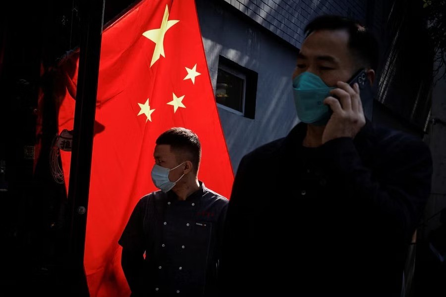 People wearing masks walk past a Chinese national flag as outbreaks of coronavirus disease (COVID-19) continue in Beijing, China, November 3, 2022. REUTERS