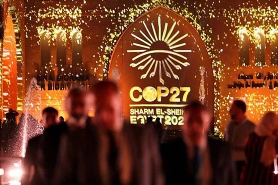 People pass in front of a wall lit with the sign of COP27 as the COP27 climate summit takes place, at the Green Zone in Sharm el-Sheikh, Egypt, Nov 10, 2022.REUTERS