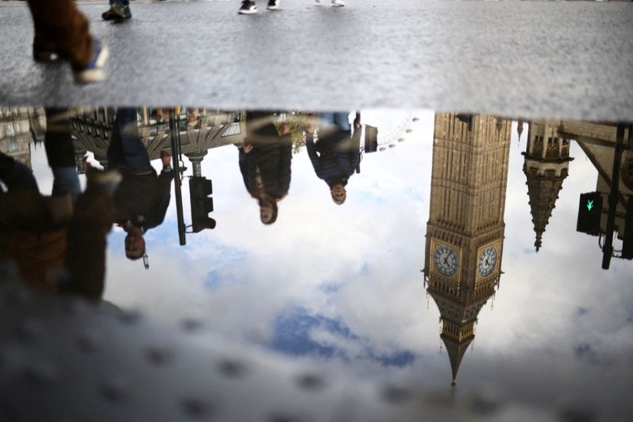 The Elizabeth Tower, more commonly known as Big Ben, is seen reflected in a puddle as people walk outside the Houses of Parliament in London, Britain, October 23, 2022. REUTERS/Henry Nicholls