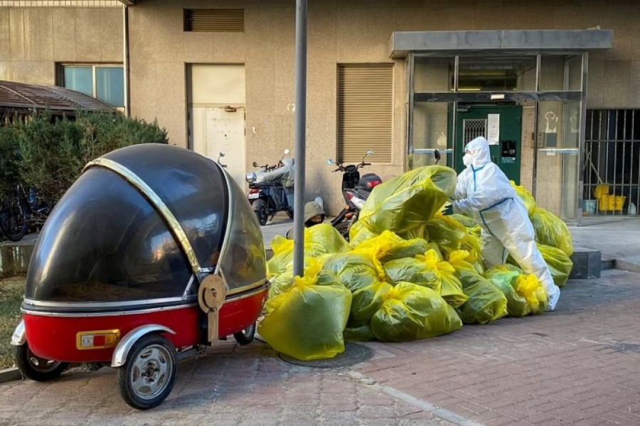 A pandemic prevention worker in a protective suit piles up bags of medical waste outside a building where residents isolate at home as coronavirus disease (COVID-19) outbreaks continue in Beijing, December 5, 2022. REUTERS