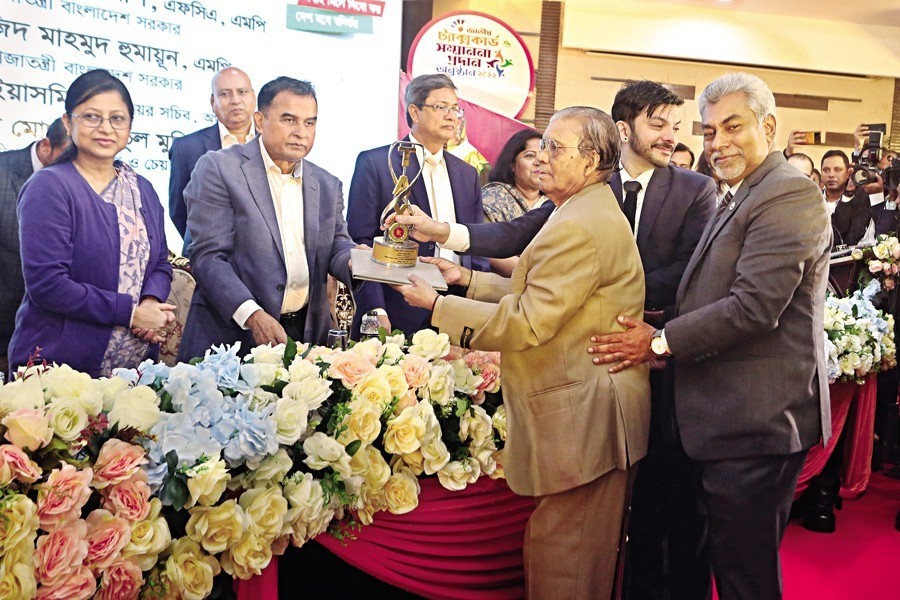 Kaus Mia, owner of Hakimpuri Zarda (processed tobacco leaves), receiving the best taxpayer award in the 'Senior Citizen' category for the fiscal year of 2021-2022 from the finance minister at a programme hosted by the National Board of Revenue (NBR) at the Officers' Club in Dhaka on Wednesday. He has been one of the highest taxpayers in the business sector since 2008. — FE photo