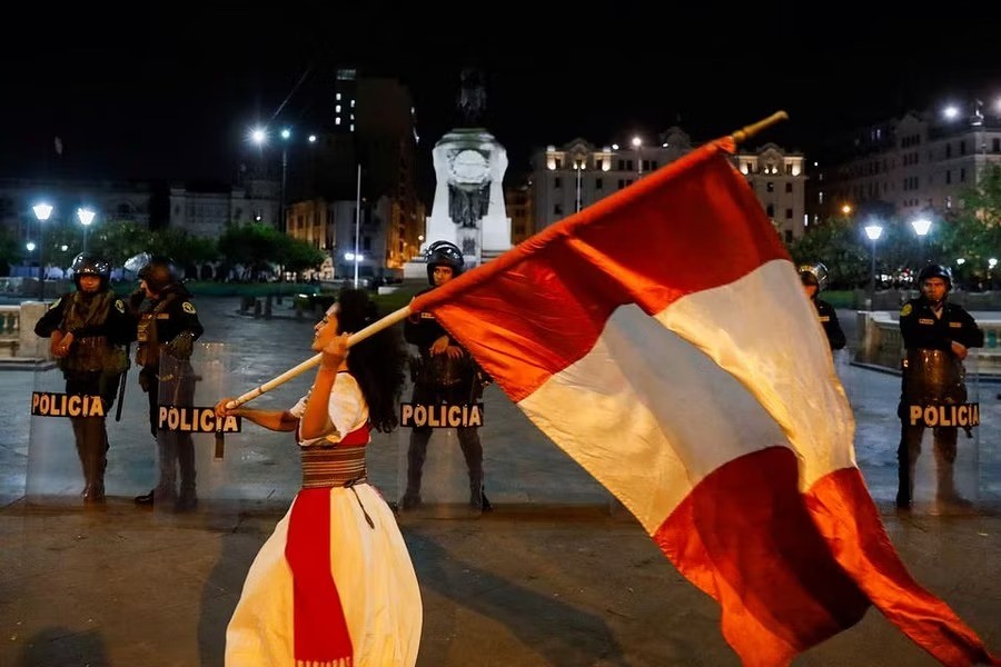 Security forces stand guard as a demonstrator waves Peru's flag during a protest to demand the dissolution of Congress and democratic elections, rejecting Dina Boluarte as Peru's president, after the ouster of leftist President Pedro Castillo, in Lima, Peru January 12, 2023. REUTERS